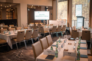 Conference room set for an investment forum with tables, chairs, water bottles, and screen.