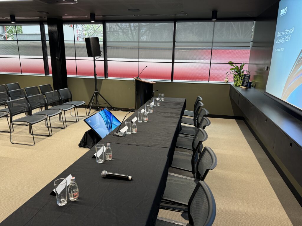 Boardroom-style setup for an Annual General Meeting, featuring a presentation screen, microphones, and a well-organized table arrangement.