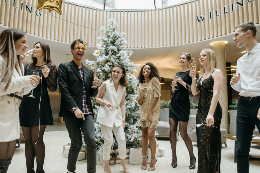 Festive group gathers around a decorated Christmas tree, holding drinks in a stylish interior.