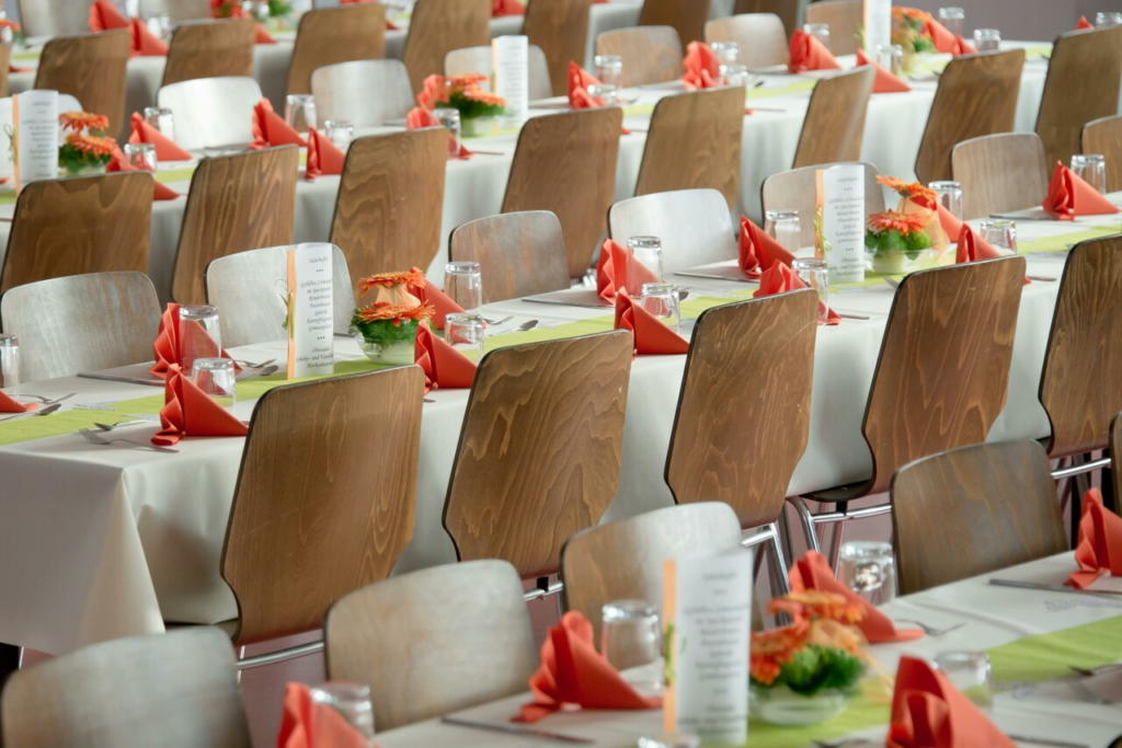 Elegantly set dining tables with folded red napkins, glassware, and floral centerpieces.