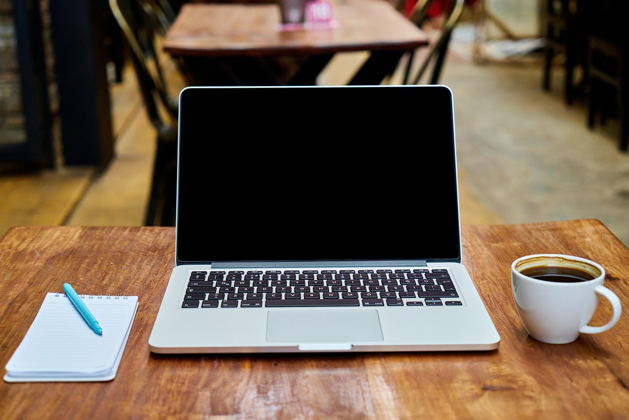 Open laptop with blank screen on a wooden table next to a notepad and coffee cup, set for a av checklist.