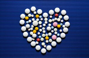 Heart-shaped arrangement of white and colorful pills on a textured blue background, styled as an event visual.