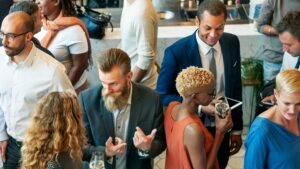 Overhead view of professionals networking at a cocktail reception in an event venue, with drinks and a tablet visible.