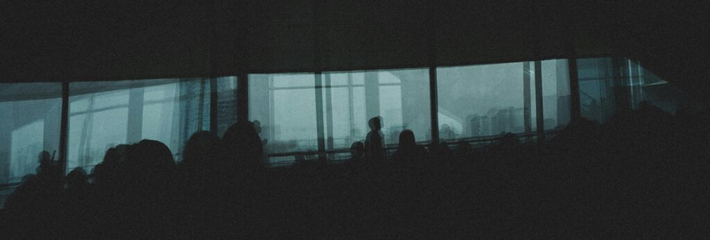 Silhouetted audience in a dim conference room with large windows revealing a foggy city skyline, backlit seating visible.