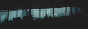 Silhouetted audience in a dim conference room with large windows revealing a foggy city skyline, backlit seating visible.