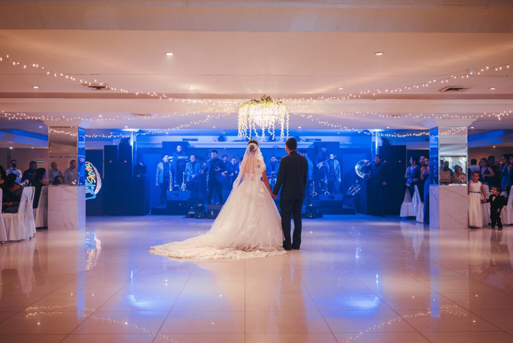 Bride and groom share their first dance at an indoor wedding reception with live band, stage lighting and twinkling ceiling lights.
